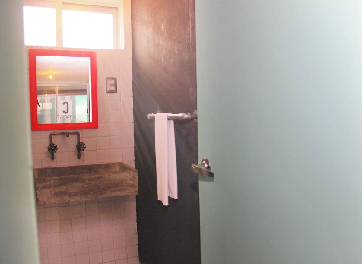 Un baño con tocador de madera, espejo con marco rojo y una toalla colgada en un perchero.