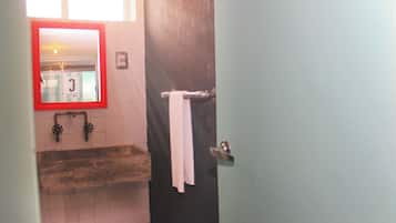 Un baño con tocador de madera, espejo con marco rojo y una toalla colgada en un perchero.