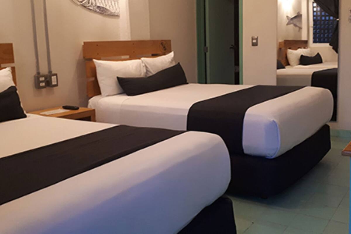 Una habitación de hotel con tres camas, un escritorio y un baño visible a través de una puerta abierta.