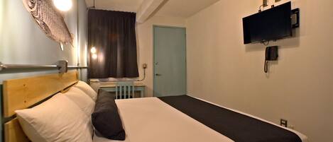 A single bed with a wooden headboard, a bedside table, a wall-mounted TV, and a light fixture shaped like a fish.