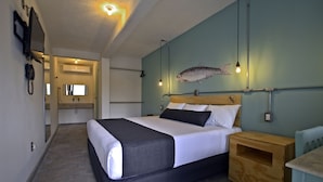 A modern hotel room with a large bed, a wooden nightstand, a small table, and a wall-mounted fish decoration.