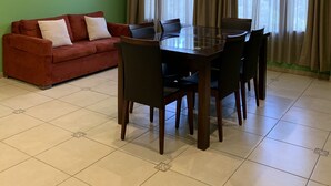 A dining area with a glass table and chairs, a red sofa, and a green wall with a framed picture. - Apart Chalten (El Calafate)