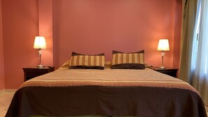 A neatly made bed with striped bedding and a green skirt, two bedside lamps, and a window with curtains. - Apart Chalten (El Calafate)