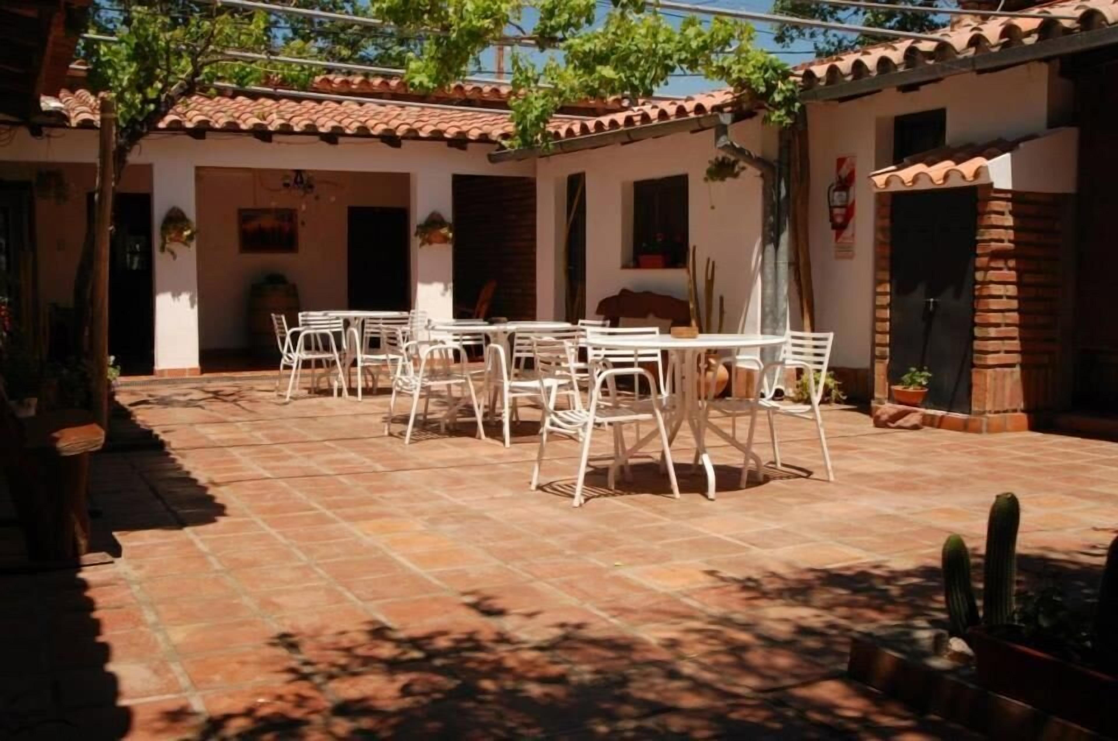 A courtyard with a tiled floor, white chairs, and a table. There are potted plants and a cactus.