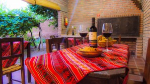 An outdoor dining area with a brick wall, a table with a colorful tablecloth, chairs, a bottle of wine, and glasses.
