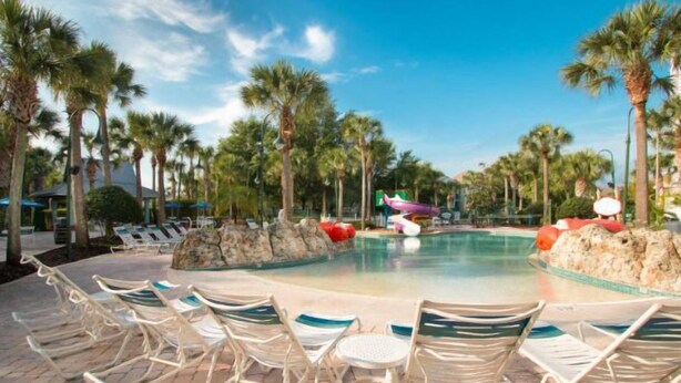 A pool area with lounge chairs, palm trees, and a water slide. - Lexington Vacations Kiss by Stark Hosp (Orlando)