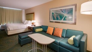 A hotel room with a bed, a sofa, a small table, and a painting on the wall. - Lexington Vacations Kiss by Stark Hosp (Orlando)
