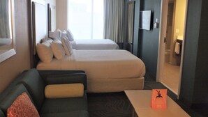 A hotel room with two beds, a sofa, a TV, and a bathroom visible through an open door. - Lexington Vacations Kiss by Stark Hosp (Orlando)