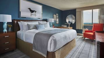 A hotel room with a large bed, two bedside tables, a desk, a chair, a mirror, and a window with a view.