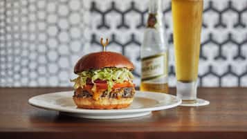A burger on a plate with a glass of beer in the background.