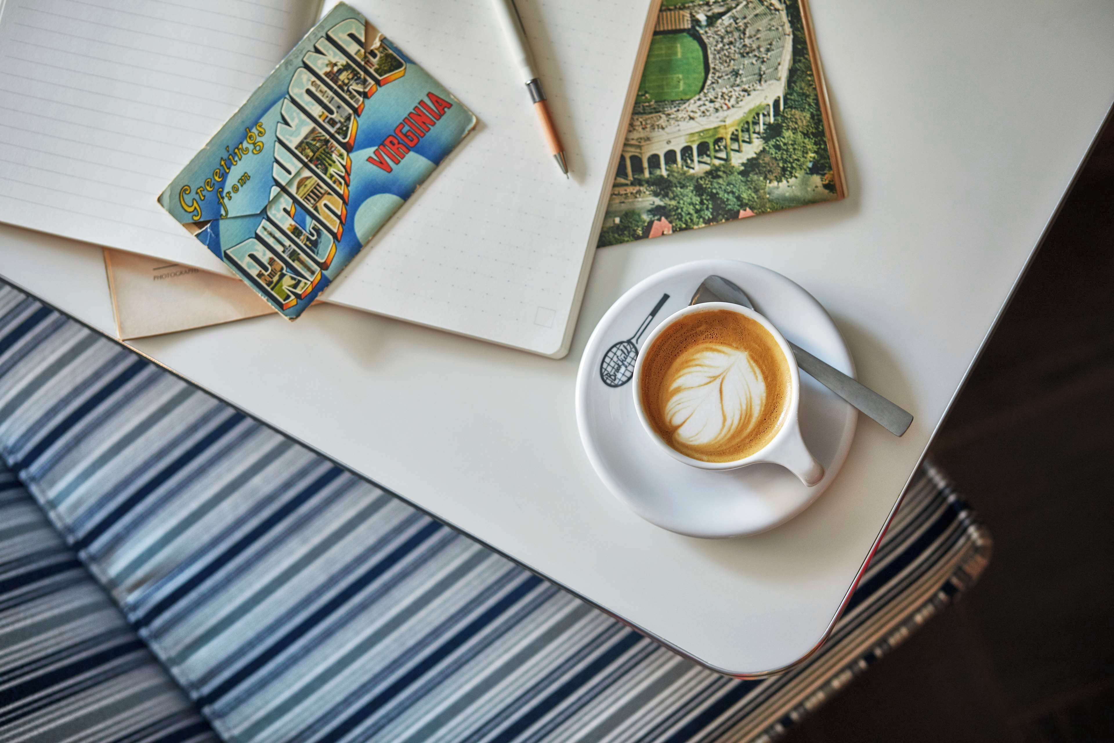 A notebook, a postcard, and a cup of coffee on a table.