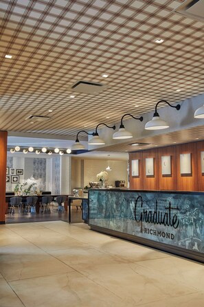 A reception area with a check-in counter labeled "Graduate Richmond," a tiled floor, and a ceiling with a grid pattern. - Graduate by Hilton Richmond (Richmond)