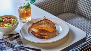 A plate with a grilled cheese sandwich, a bowl of salad, and a glass of iced tea on a tray.
