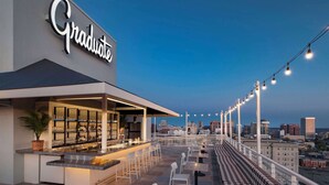 An outdoor bar area with a city skyline view, a 'Graduate' sign, and outdoor seating. - Graduate by Hilton Richmond (Richmond)