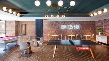 A billiards room with a pool table, chairs, and a neon sign displaying a phone number.