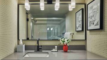 Un baño moderno con un espejo grande, un lavabo, un florero rojo con flores y obras de arte enmarcadas en la pared.