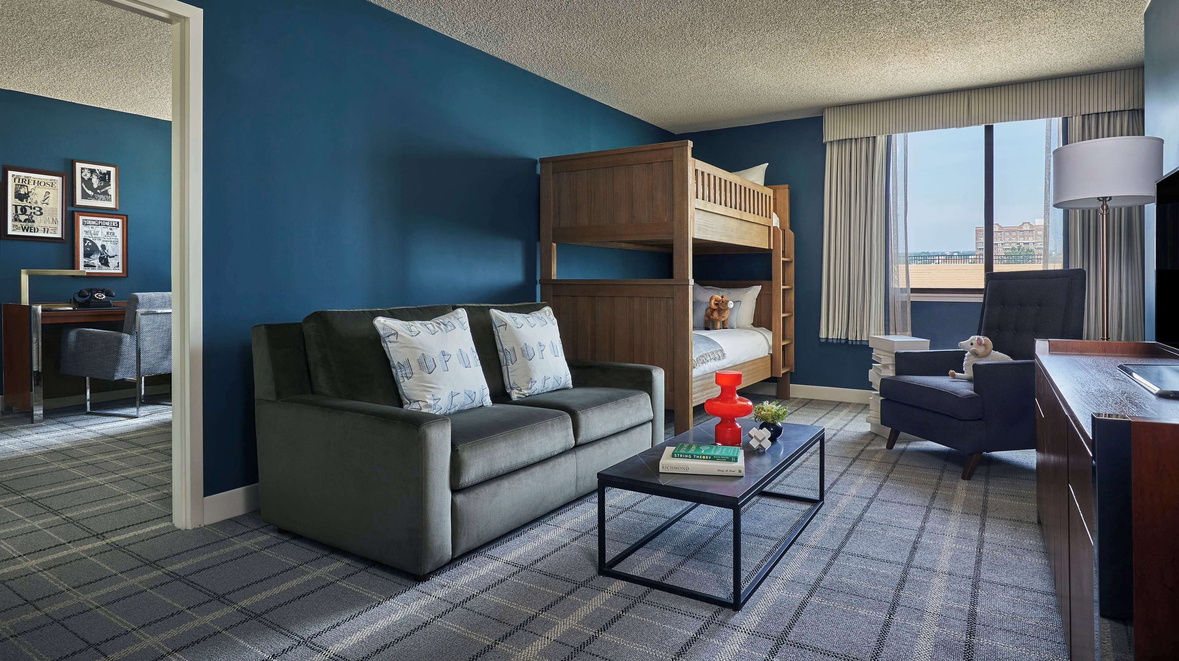 Ein Hotelzimmer mit Etagenbett, einer Schlafcouch, einem Schreibtisch und Blick auf die Stadt.