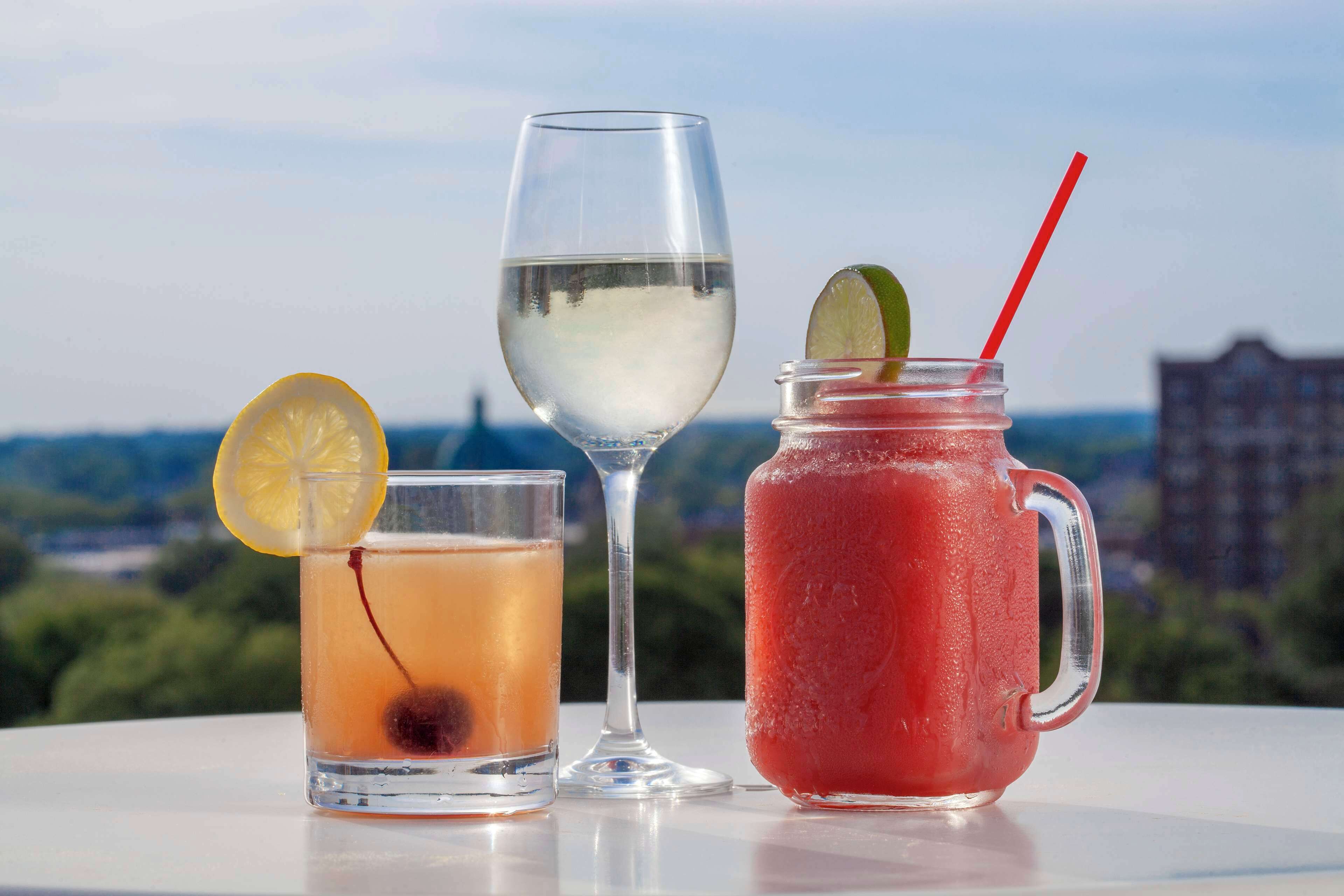 Tres bebidas sobre una mesa con vista a la ciudad al fondo.