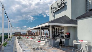 An outdoor seating area with white chairs and tables, a bar, and a view of the city skyline. - Graduate by Hilton Richmond (Richmond)