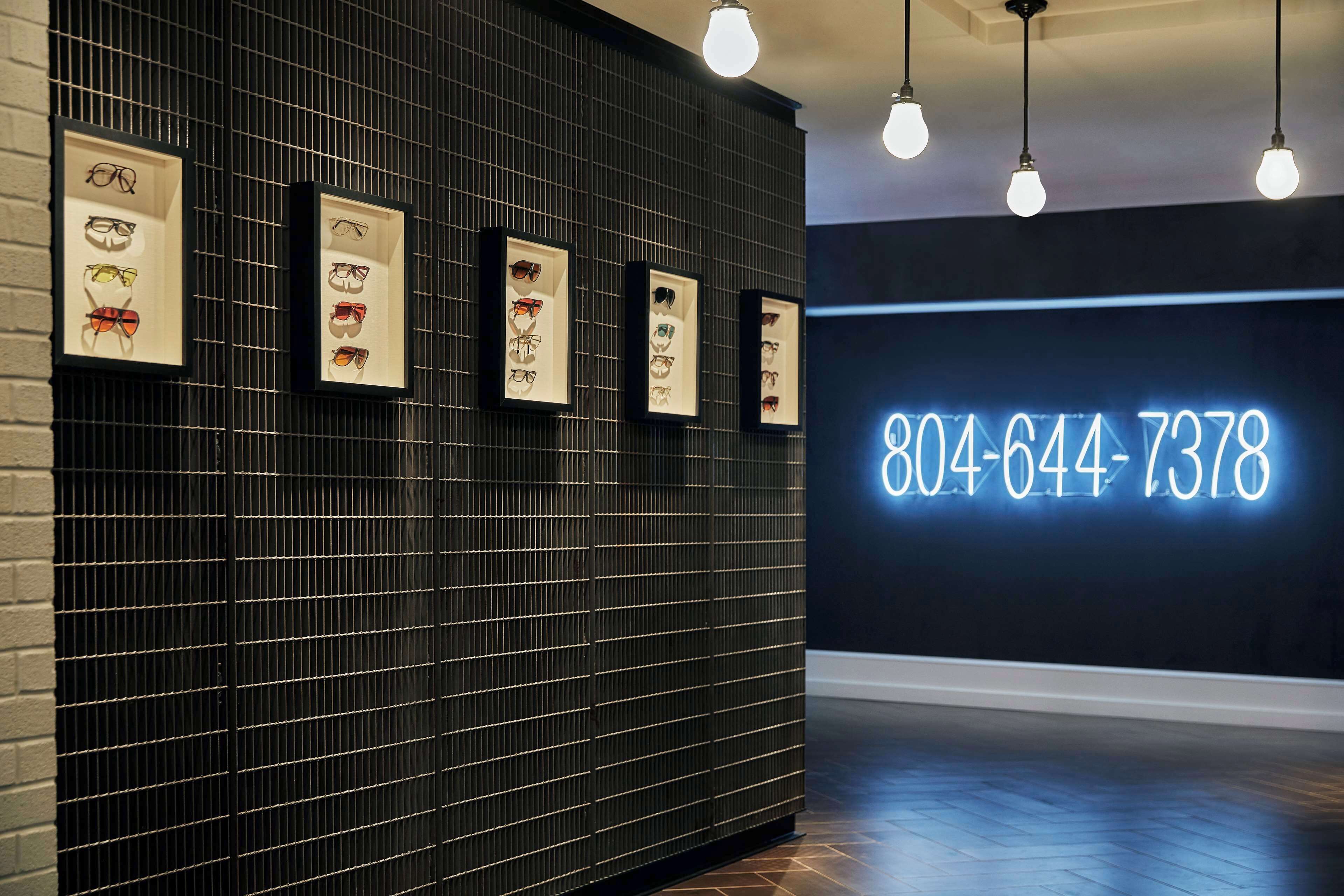 A wall with framed eyewear displays and a neon sign with a phone number.