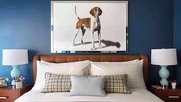 A bedroom with a large bed, two bedside tables with lamps, a framed picture of a dog on the wall, and a blue wall.