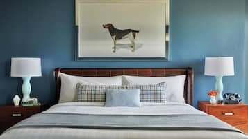 Una cama bien hecha con cabecera, dos mesitas de noche con lámparas, y un cuadro de un perro en la pared.