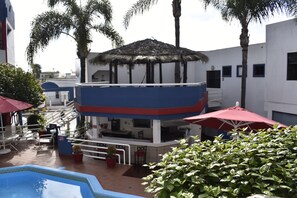 Un área de piscina con una estructura de techo de paja, asientos exteriores y palmeras.