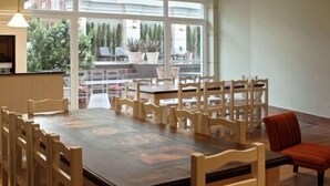 A dining area with a large table and multiple chairs, a small kitchen area, and large windows offering a view of the outdoors. - Las Piedras Beach Experience I (Mar del Plata)