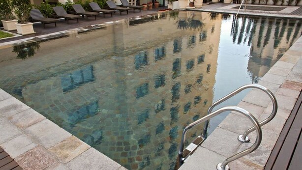 Una piscina cristalina con una escalera metálica, sillas de descanso y plantas en macetas alrededor del borde.