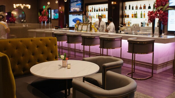 A bar area with a round table, bar stools, and a counter with a bartender. - Villa Arden Hills (Sacramento)