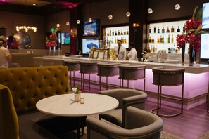 A bar area with a round table, bar stools, and a counter with a bartender. - Villa Arden Hills (Sacramento)