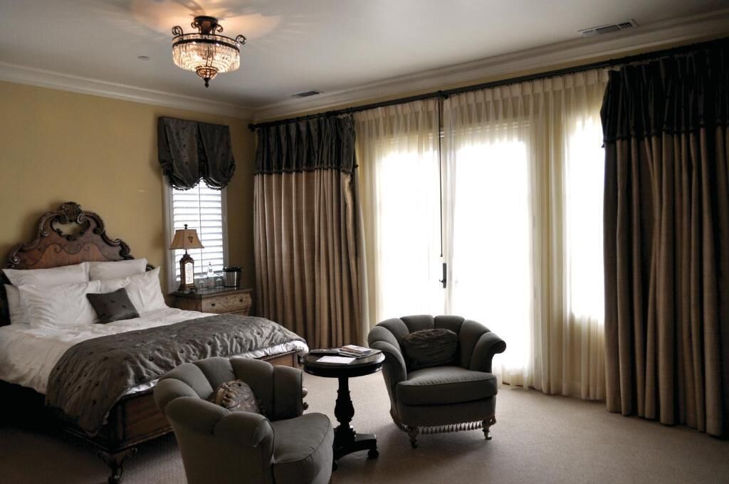 Ein Hotelzimmer mit einem großen Bett, zwei Sesseln, einem kleinen Tisch, einer Kandelaberleuchte und Vorhängen.