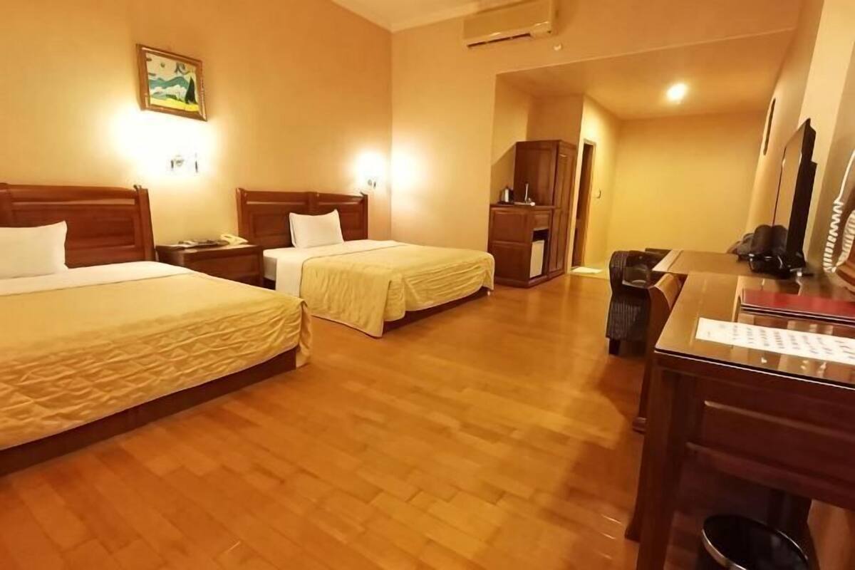 A hotel room with two beds, a desk, a chair, a television, and a small kitchenette.