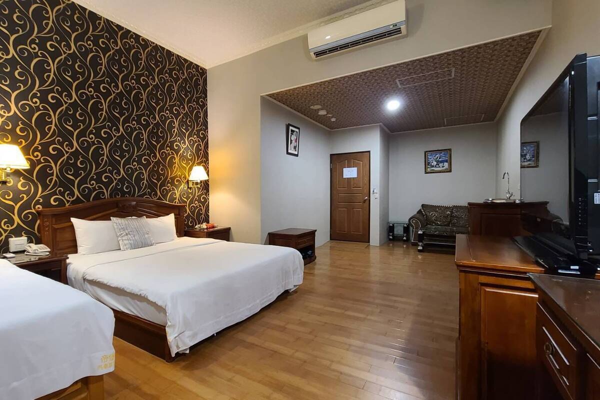 A hotel room with two beds, a wooden desk, a television, and a patterned wallpaper.