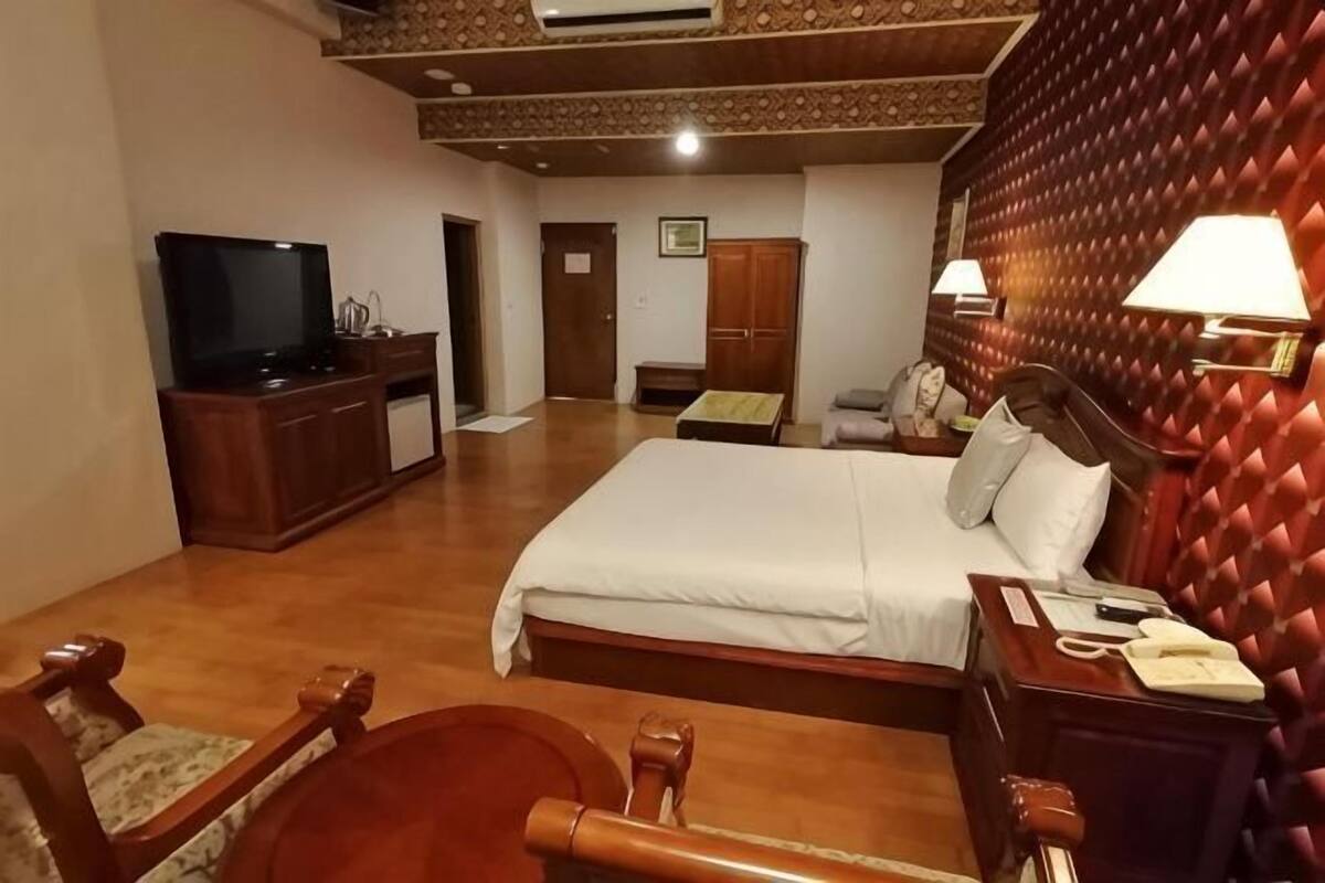 A hotel room with a bed, a TV, a desk with a phone, a chair, and a wardrobe.