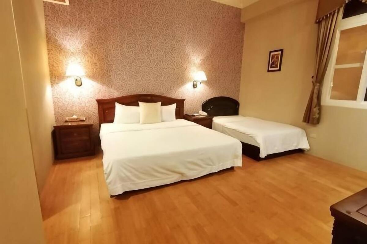 A hotel room with two beds, wooden flooring, and wall-mounted lights.