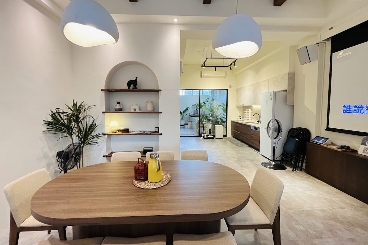A modern dining area with a wooden table and chairs, pendant lights, and a view into the kitchen.