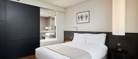 A modern hotel room with a large bed, a bedside table, a nightstand, and a large window.