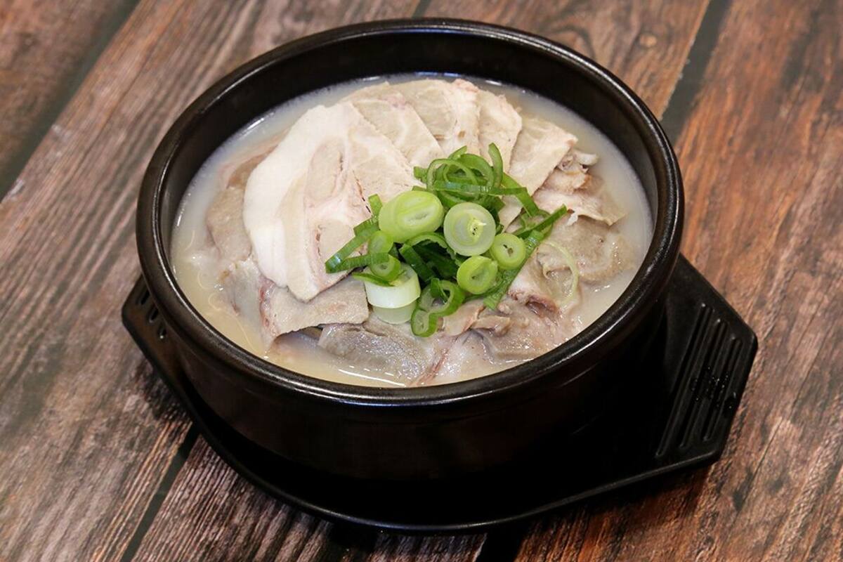 A bowl of soup with sliced meat and green onions on a wooden table.