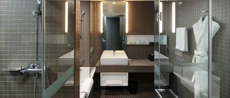 Un baño moderno con ducha envuelta en vidrio, un lavamanos amplio y un espejo.