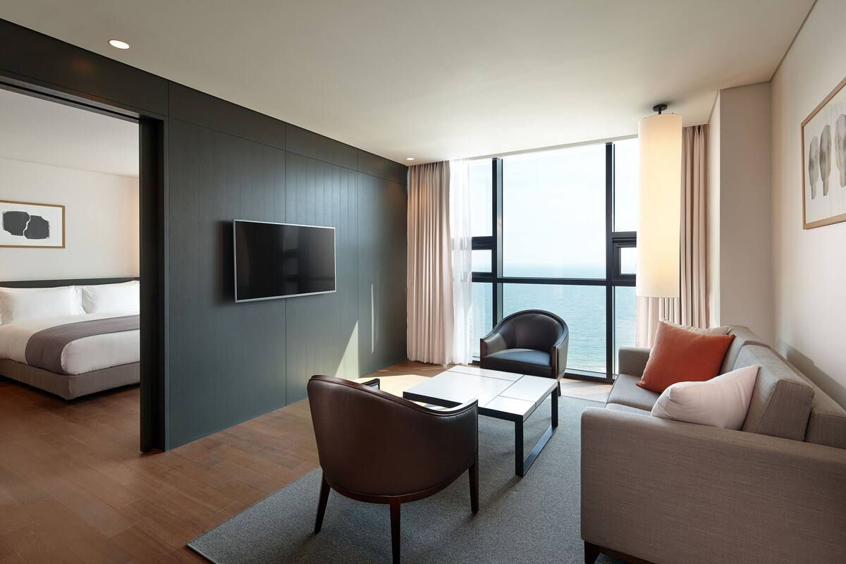 A modern hotel room with a bed, a TV, a sofa, and a dining table.