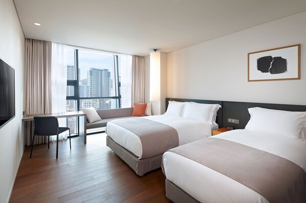 Habitación de hotel con dos camas, un escritorio y un amplio ventanal con vista a la ciudad.