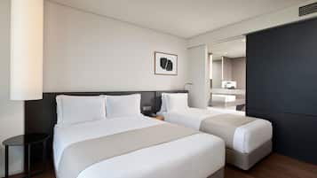 Habitación de hotel con dos camas, una mesita de noche, una lámpara, un espejo y un cuadro en la pared.