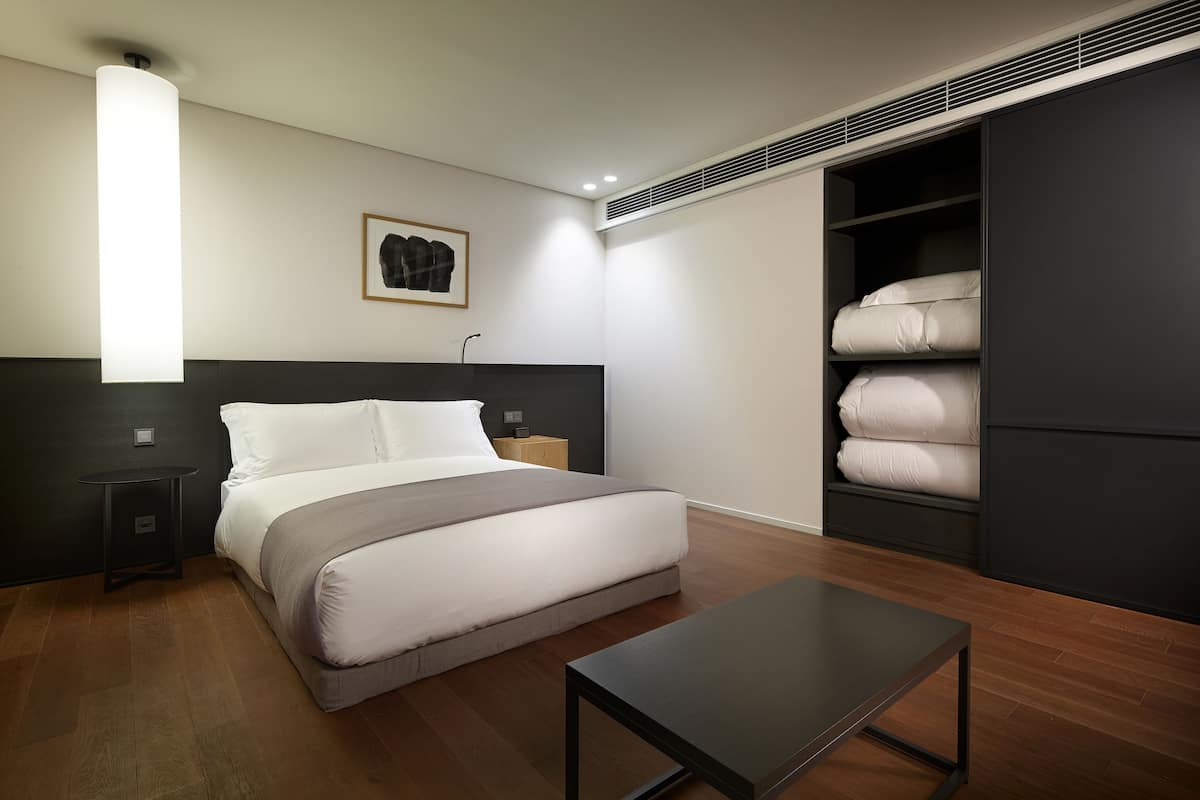 A modern bedroom with a bed, bedside tables, a bedside lamp, a wardrobe, and a small table.