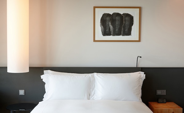 Habitación de hotel con cama, mesita de noche, una obra de arte en la pared y una lámpara moderna.