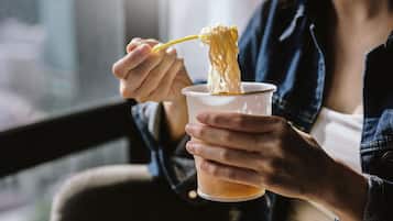 A person holding a cup with noodles and a yellow spoon.