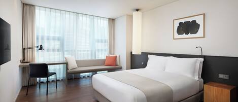 Una habitación de hotel moderna con una cama grande, un escritorio con una silla, un banco y un ventanal con cortinas translúcidas.