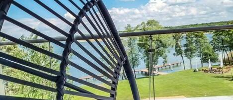 A hammock chair overlooking a lake with a grassy area and a wooden deck.