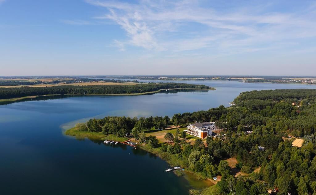 Ejendom ved søen med en stor bygning, bådebro og omkringliggende skov.