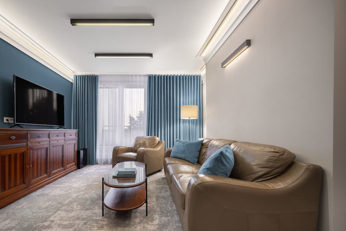 A modern living room with a leather sofa, a glass coffee table, a TV, and a large window with curtains.